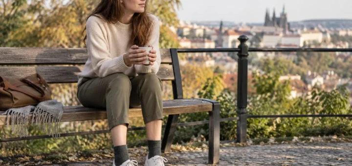 Žena sedí na lavičce v kotníkových kalhotách s jednobarevnými ponožkami